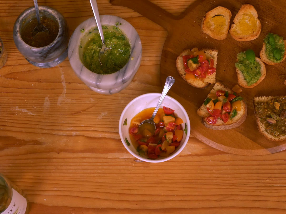 Toasted bruschetta topped with tomatoes, basil pesto and pistachio pesto beside marble mortars of fresh pesto.